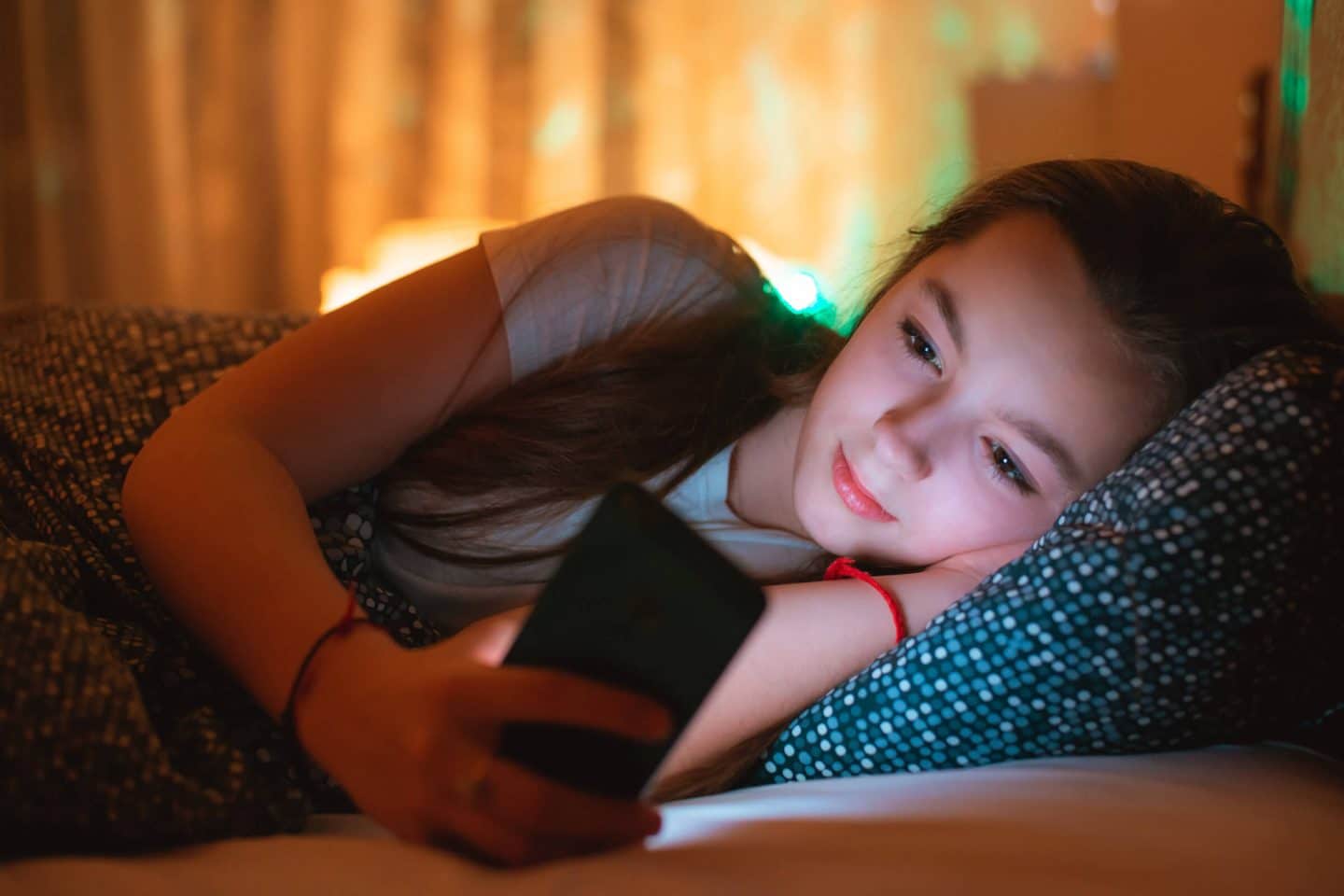 Teen girl lying in bed with phone