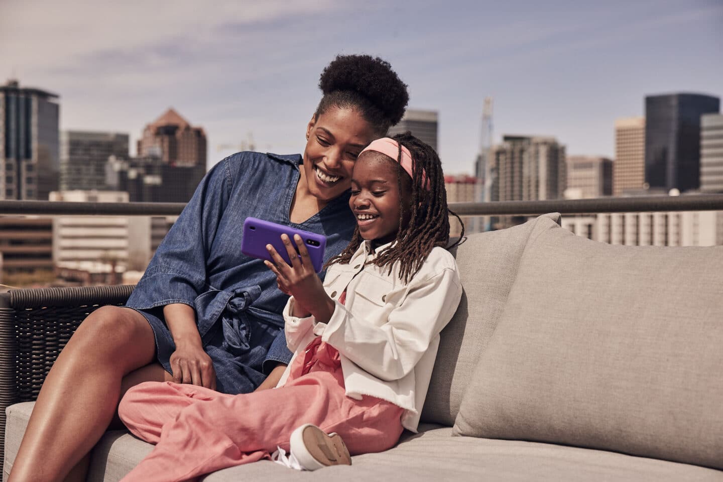 African American mom and daughter smiling and taking a selfie together on a rooftop with a city skyline in the background