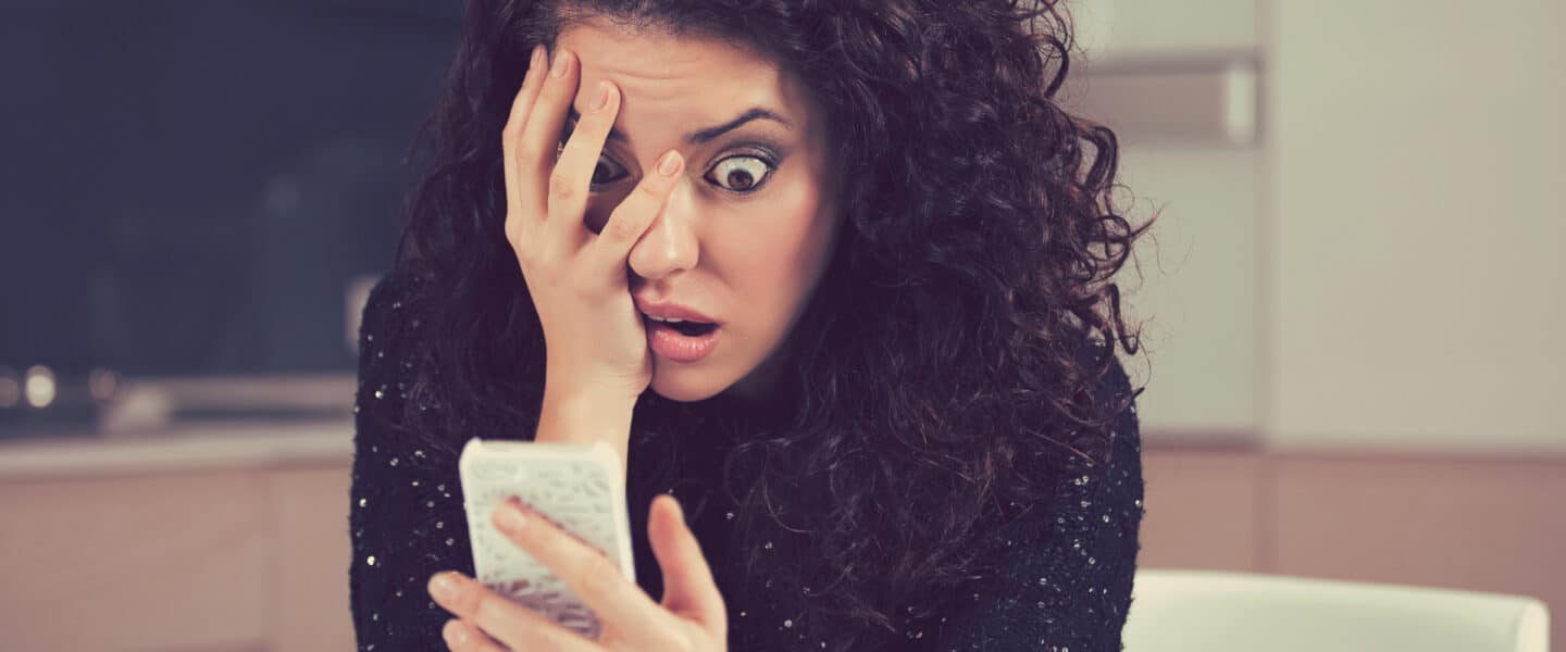 Shocked anxious woman looking at phone seeing something bad
