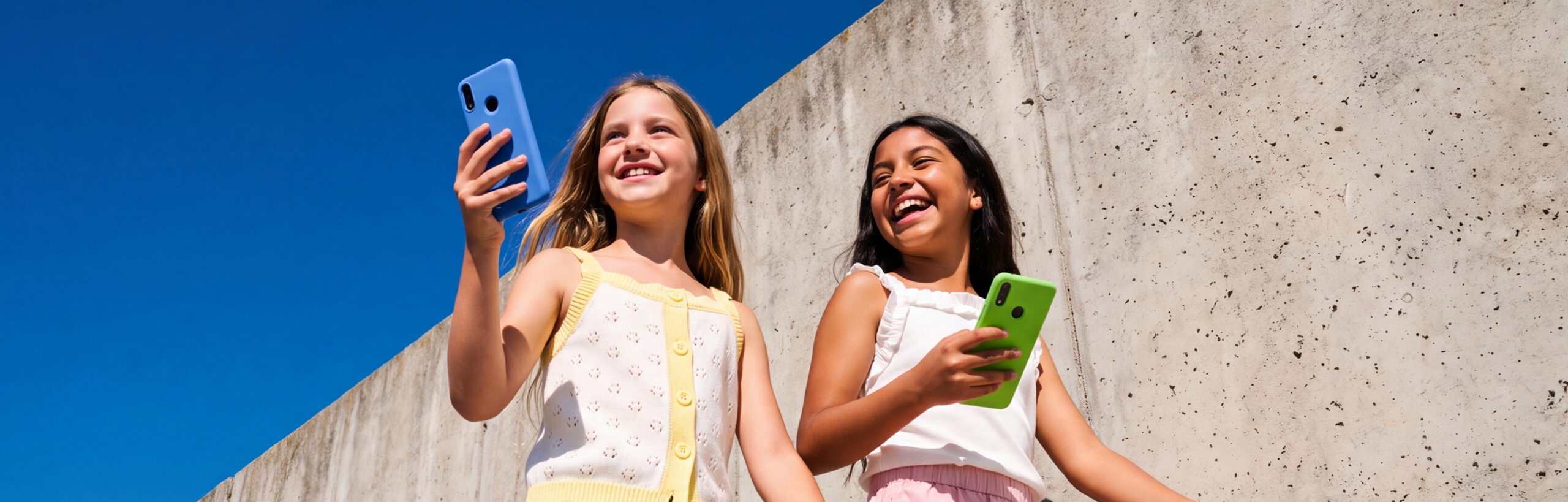 Two young girls walking outside and laughing while holding Gabb phones